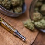 Cannabis Oil Vape Pen & Marijuana Buds In Open Glass Jar In Background